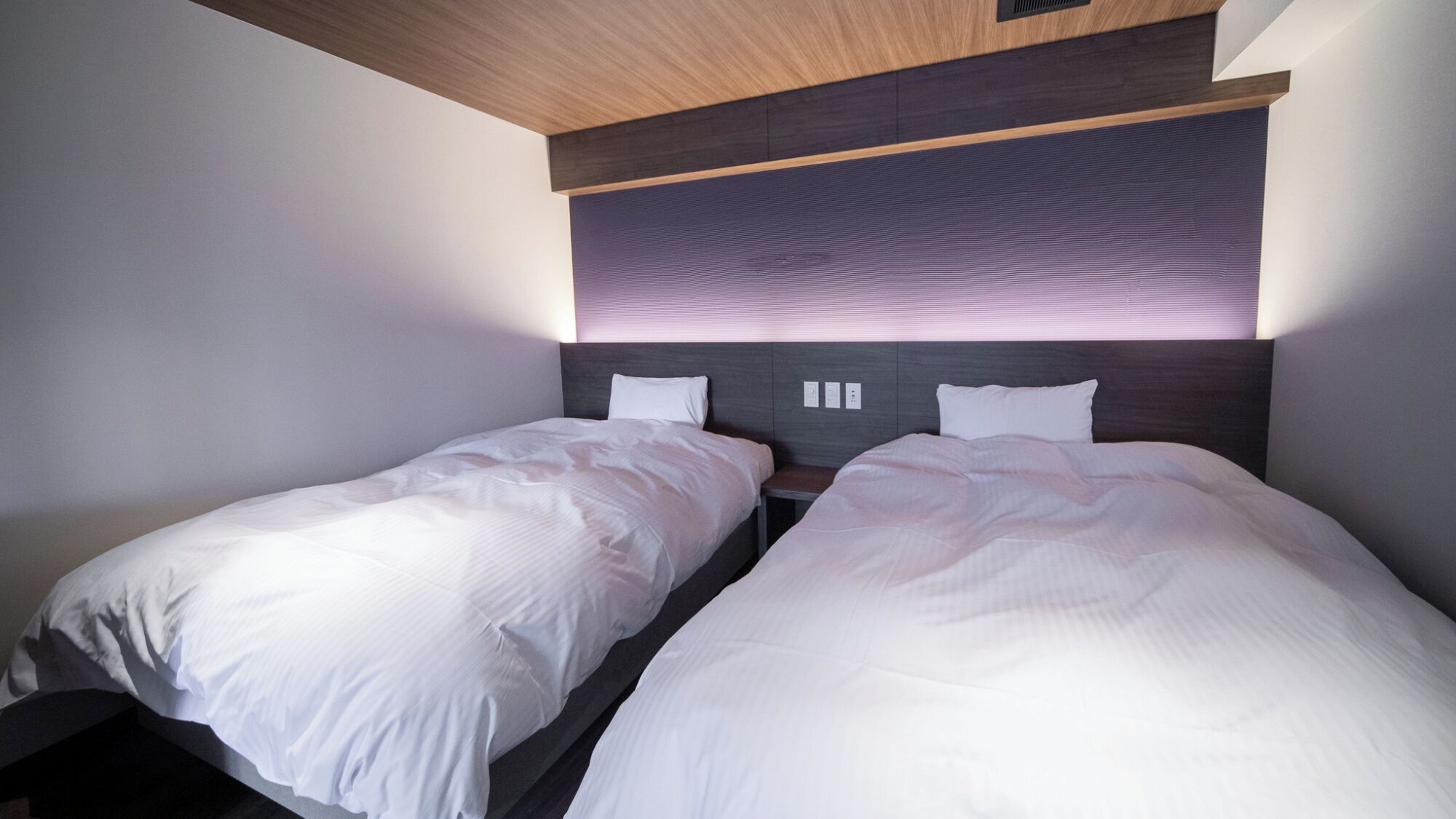 Ein modernes Hotelzimmer mit zwei Einzelbetten, einer Holzbalkendecke und einer fest installierten Kopfteil.