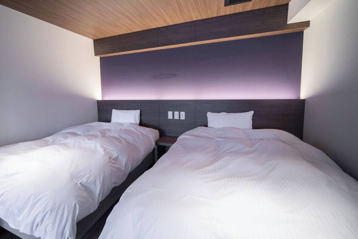 Quarto de hotel moderno com duas camas de solteiro, teto de madeira e cabeceira embutida.