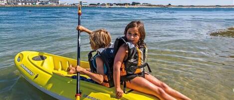 Dos personas en un kayak amarillo sobre aguas claras, con una orilla lejana.