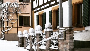 Una escalera cubierta de nieve que lleva a un edificio con fachada tradicional, que incluye una barandilla de piedra y un ventanal con marco de madera.