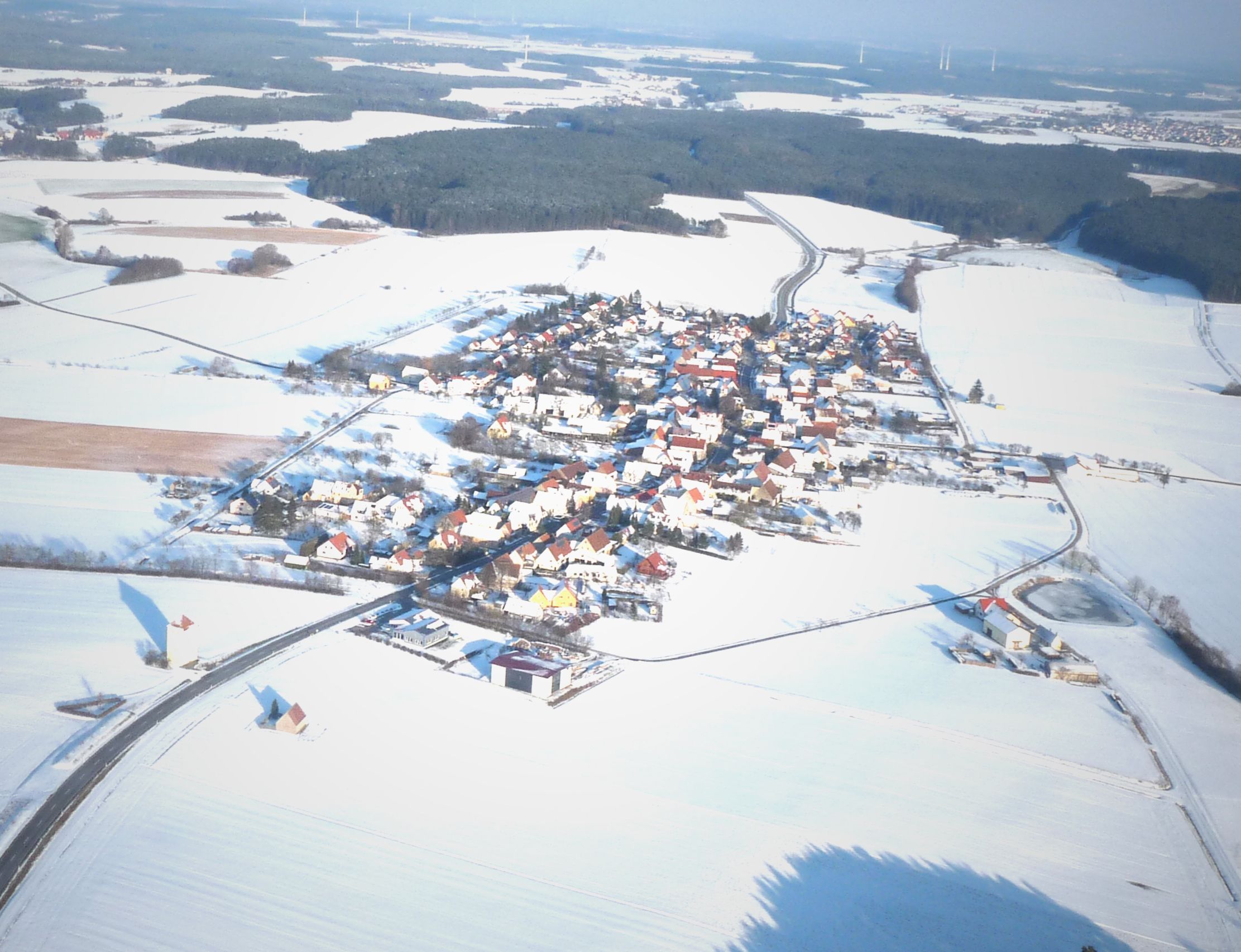 An aerial view of a snow-covered village with houses and roads.