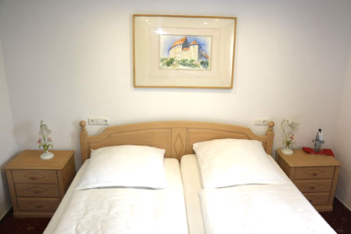A double bed with two nightstands, one with a vase and the other with a bottle.