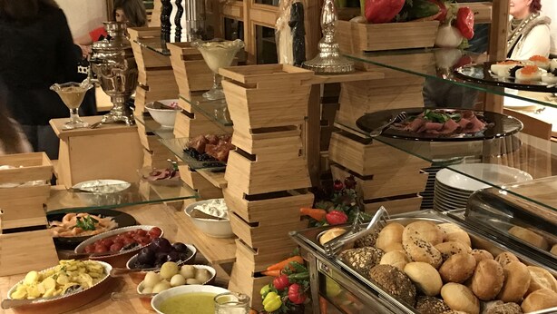 Un bufé con distintos alimentos, como carnes, quesos y frutas, dispuestos en puestos de madera y vitrinas de vidrio.
