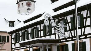 Un edificio tradicional con entramado de madera, fachada cubierta de nieve y una torre del reloj al fondo.