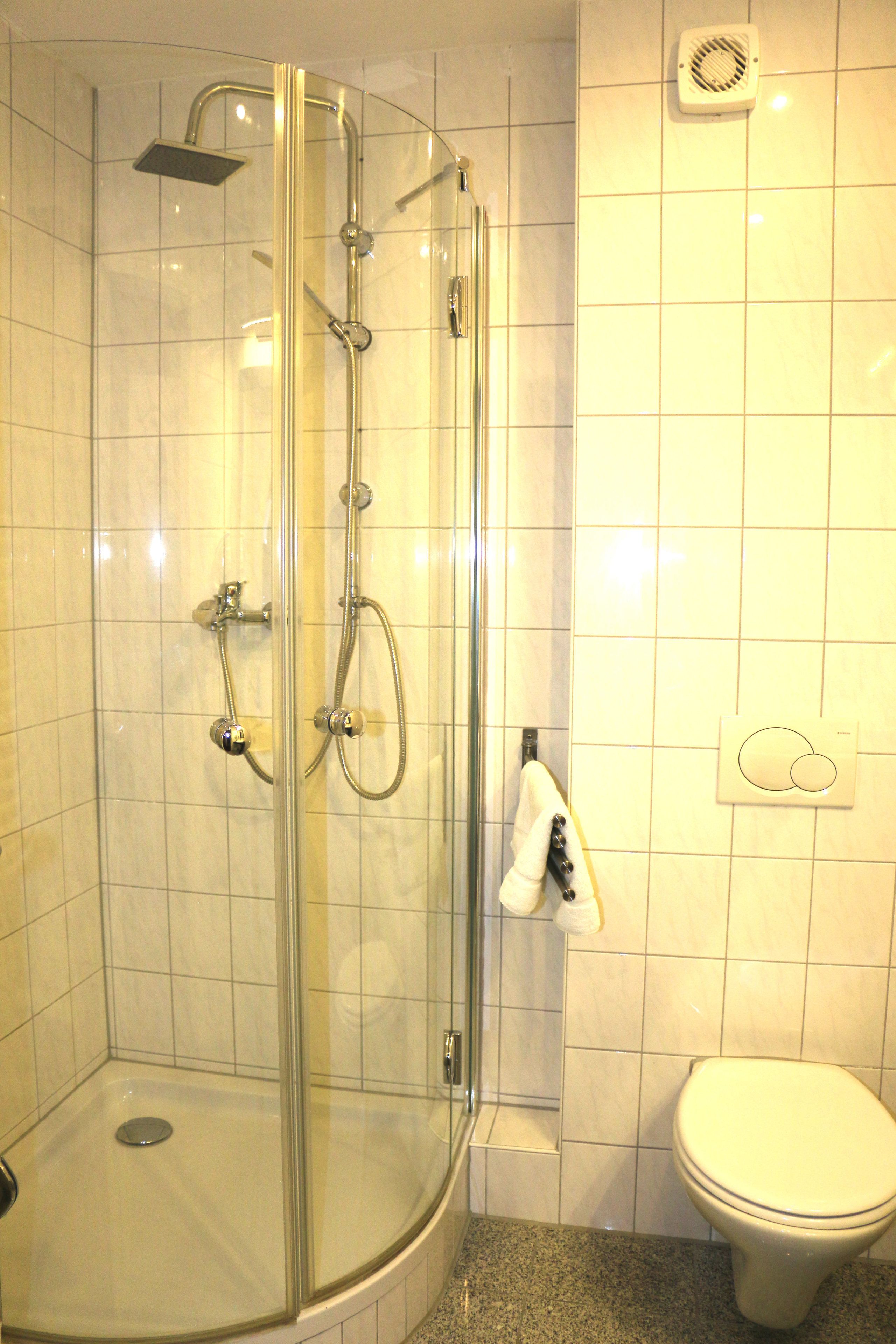 A glass-enclosed shower with a handheld showerhead and a wall-mounted faucet.