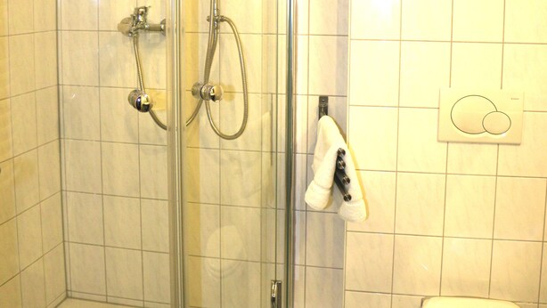 Une douche fermée par des parois en verre, dotée d’un pommeau de douche à main et d’un robinet mural.