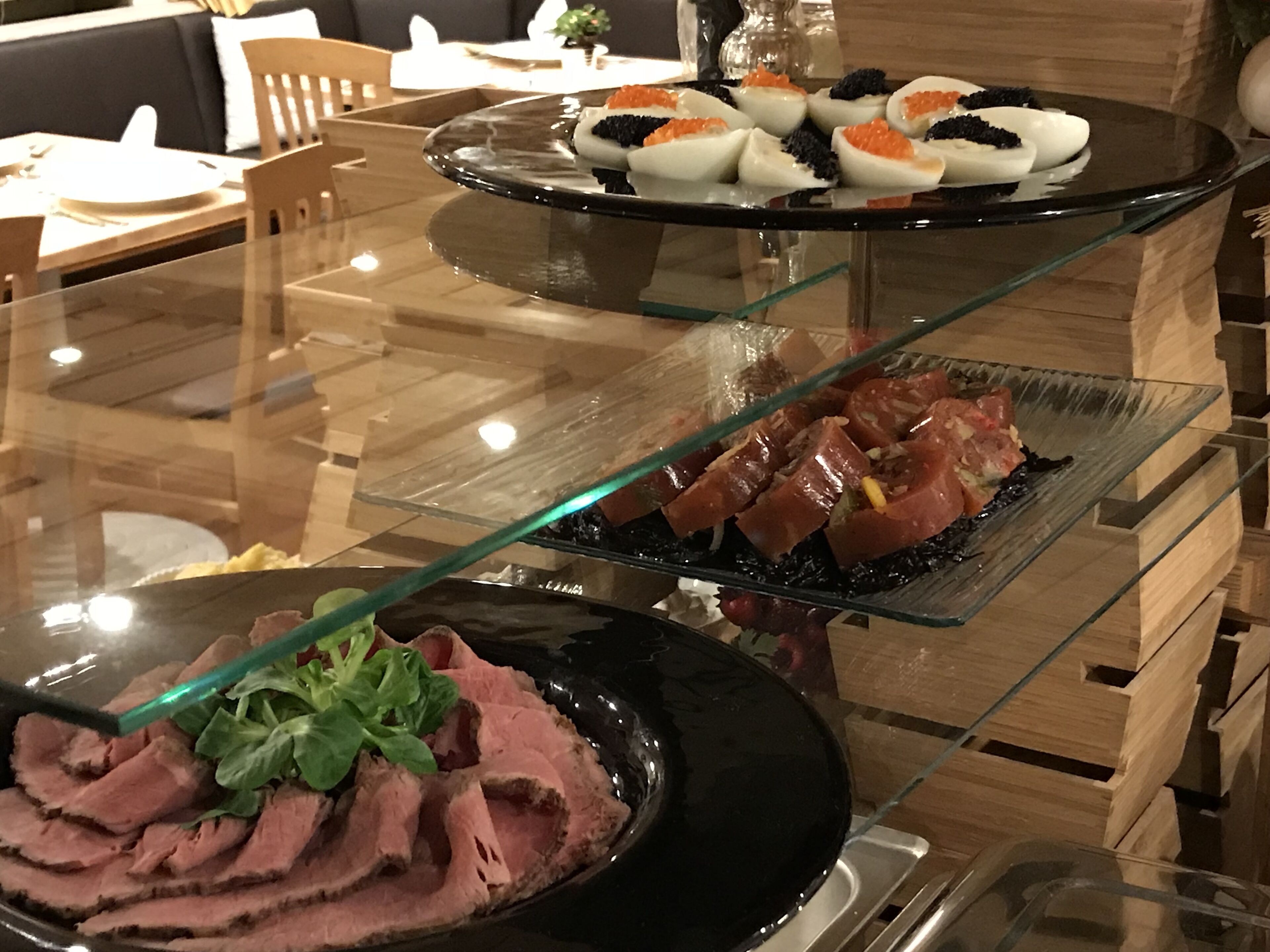 Une table à manger avec un plateau en verre, sur laquelle sont disposés trois plats de nourriture présentés sur des assiettes en verre.