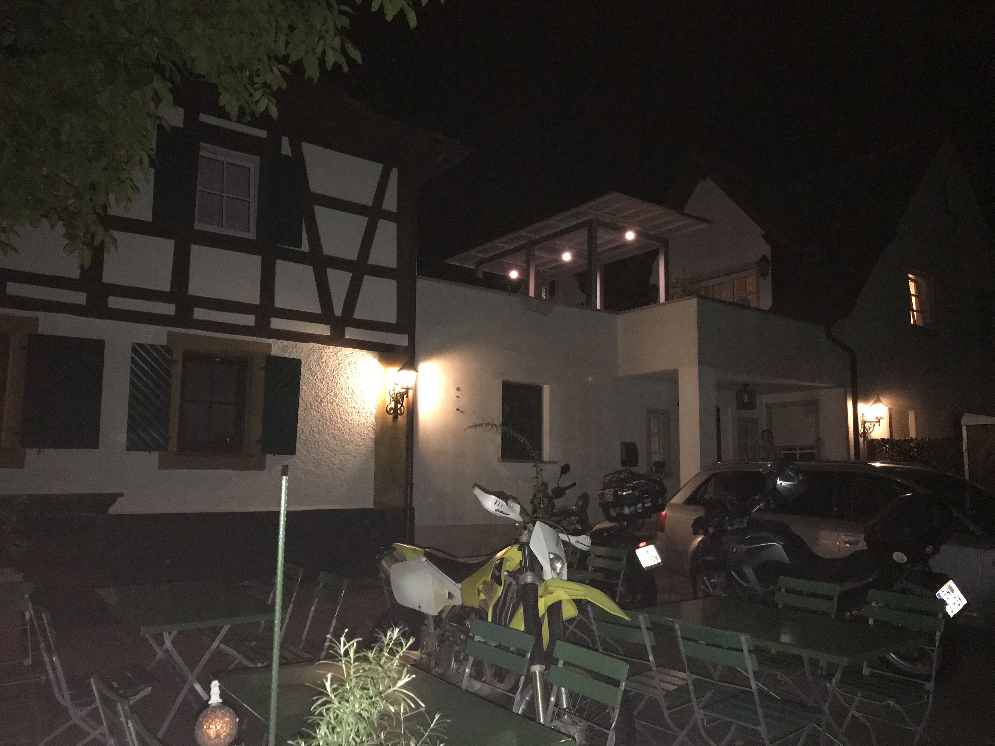 A two-story building with a balcony, a parked motorcycle, and a car in the driveway.