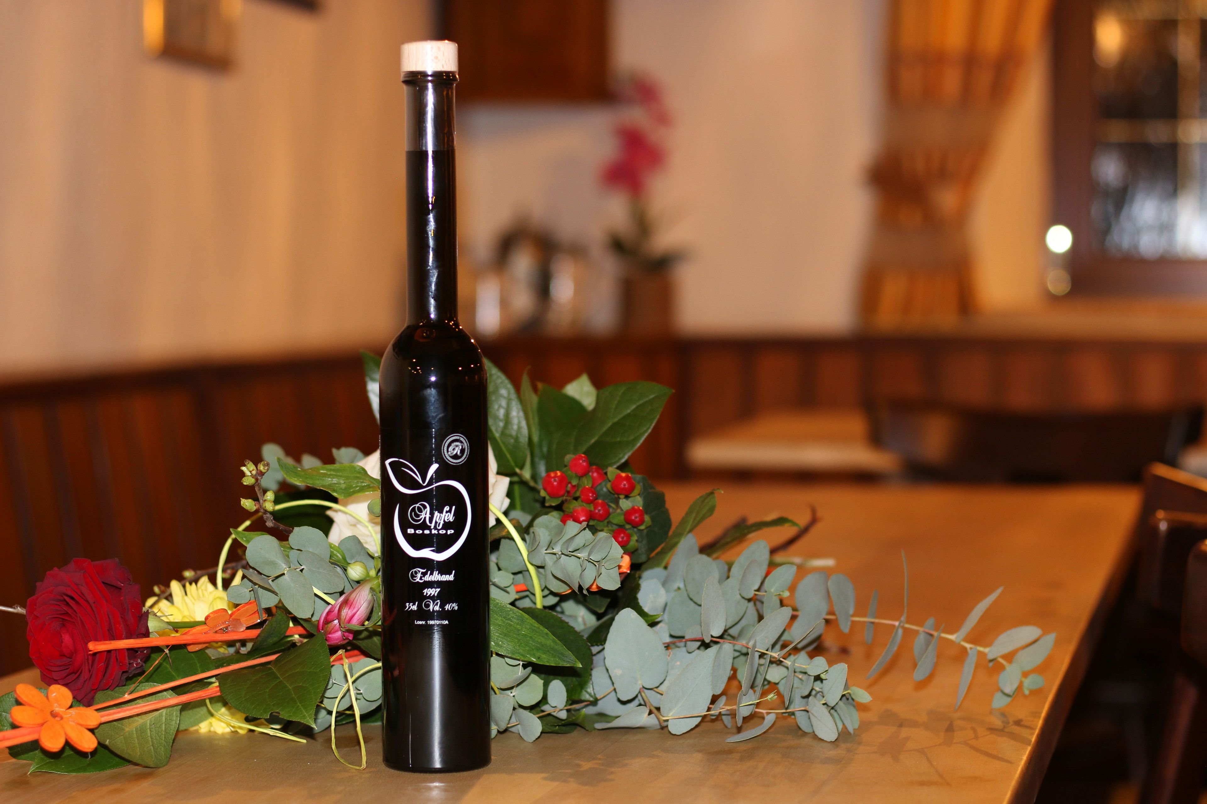 Uma garrafa de vinho com etiqueta, colocada sobre uma mesa com arranjo de flores.