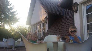 Dos niños sentados en una mesa al aire libre, con una casa al fondo.