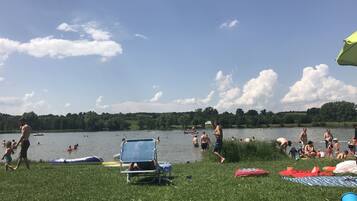 A grassy area with a lake, people swimming, and a boat in the distance.