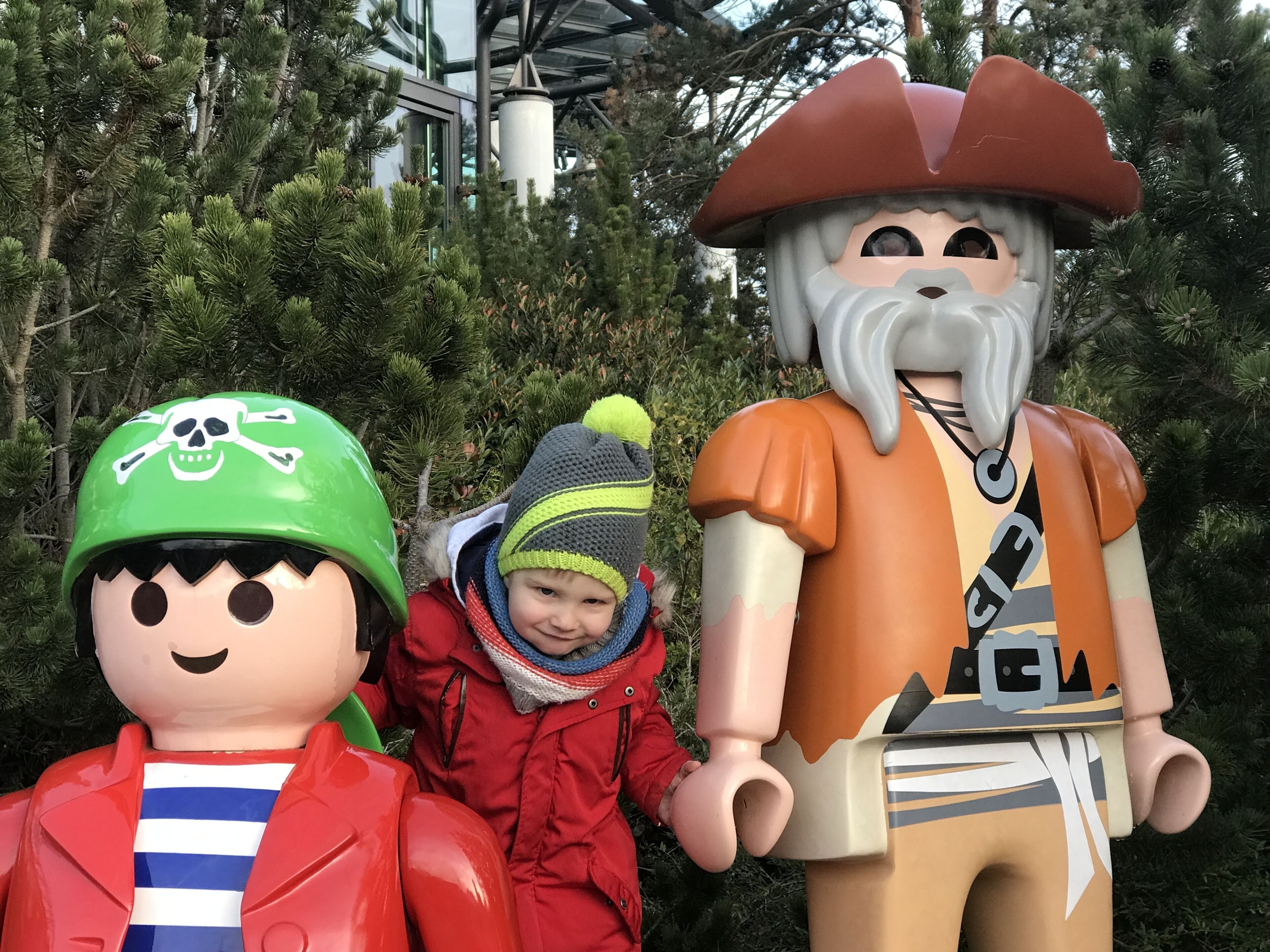 Criança com casaco vermelho e uma estátua de pirata com barba e chapéu.