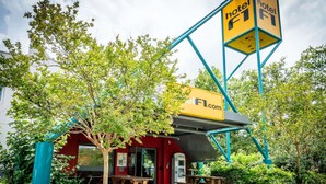 A hotel with outdoor seating, a signboard, and a tree in front. - hotelF1 Brive Ussac (Ussac)
