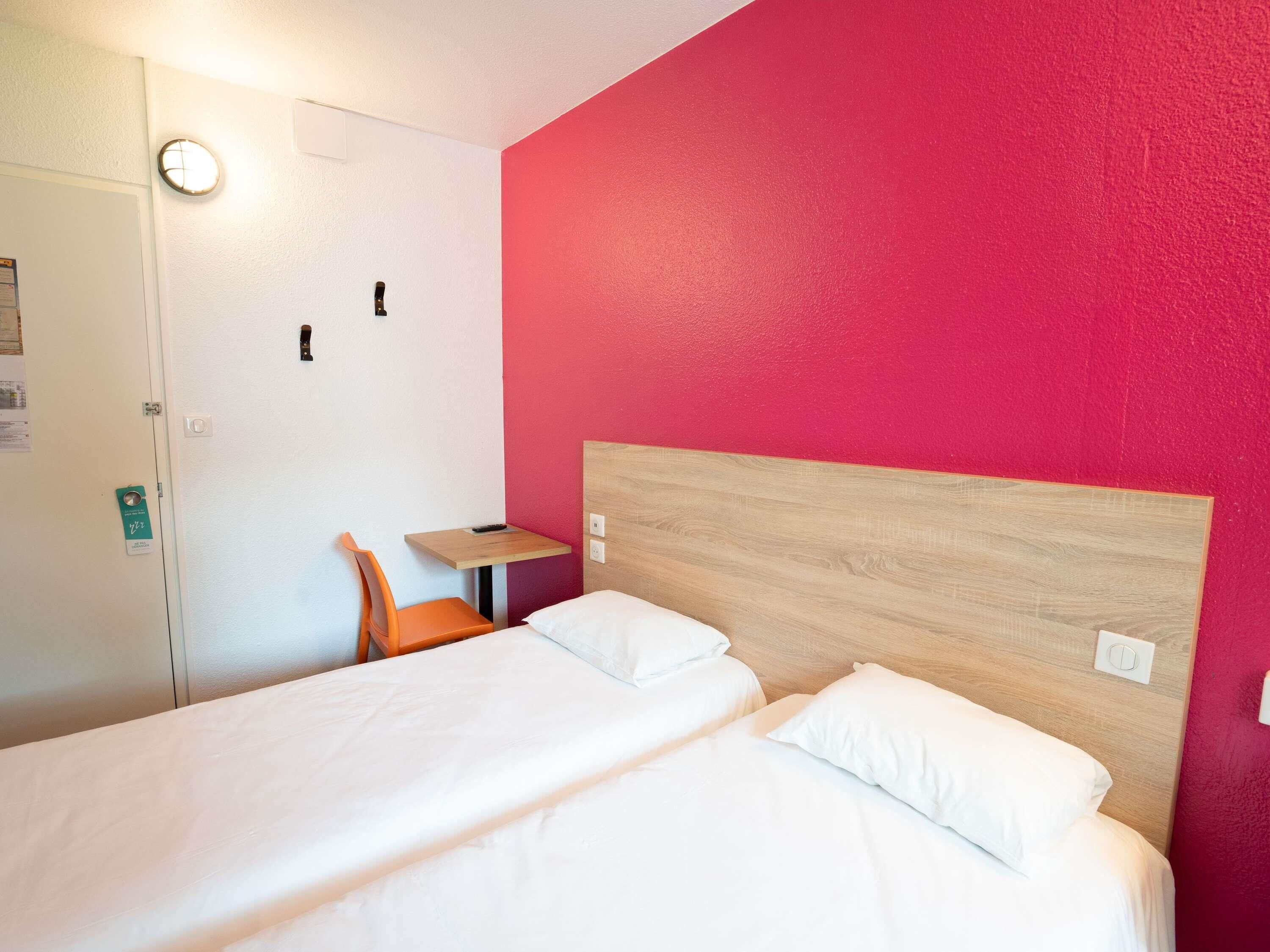 Een hotelkamer met een bed, een klein tafeltje, een oranje stoel en een rode muur.