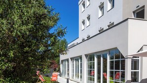 An outdoor seating area with orange chairs and tables, a building with large windows, and a clear blue sky. - ibis budget Strasbourg Sud Illkirch Geispolsheim (Geispolsheim)