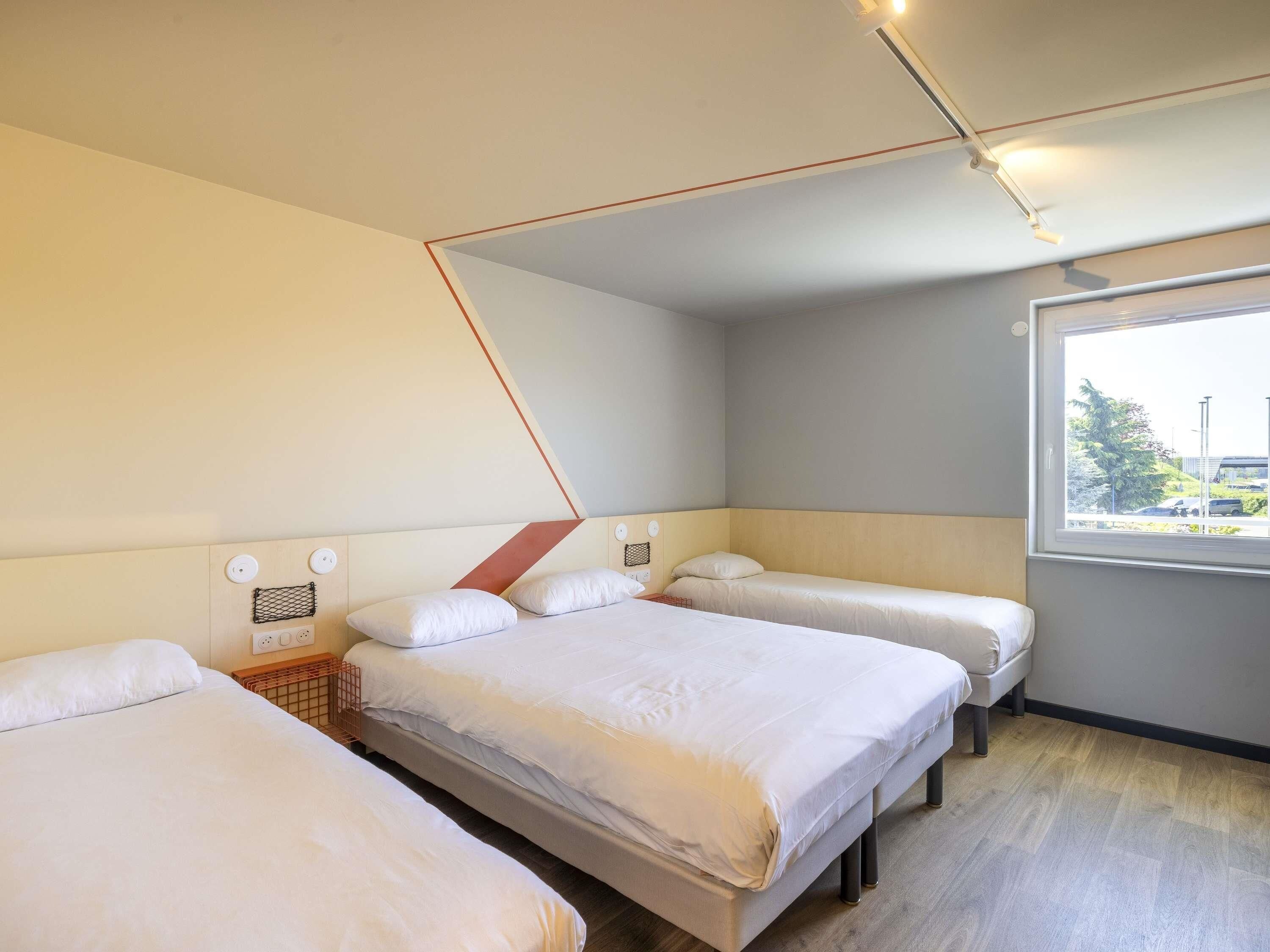 A hotel room with three beds, a window with a view, and a geometric ceiling design.