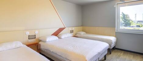 A hotel room with three beds, a window with a view, and a geometric ceiling design.