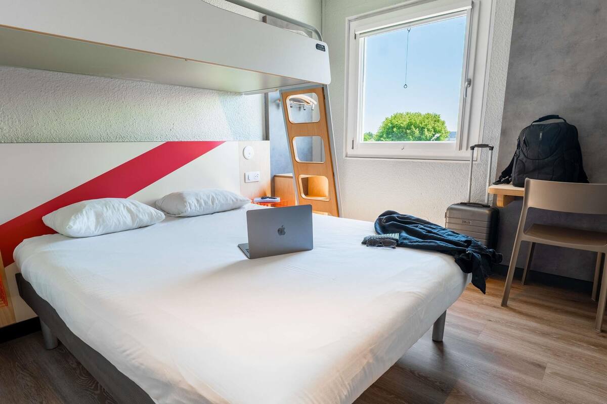 Habitación de hotel moderna con una cama, una computadora portátil, una maleta y vistas a zonas verdes.