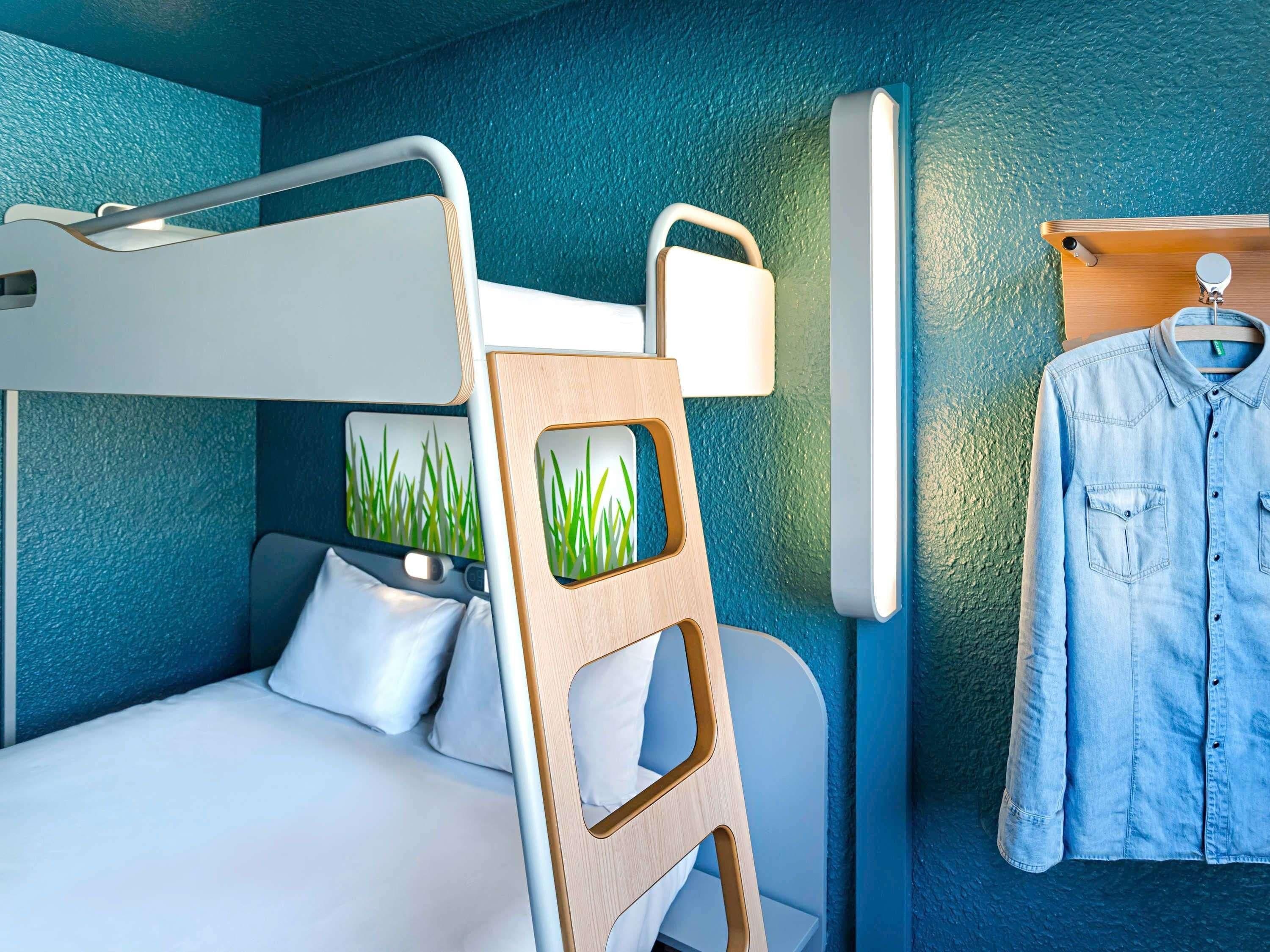 Una cama litera con escalera, una lámpara colgante y una camisa vaquera en un perchero.