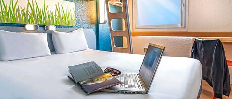 A hotel room with a bed, a laptop, a pair of glasses, and a window.