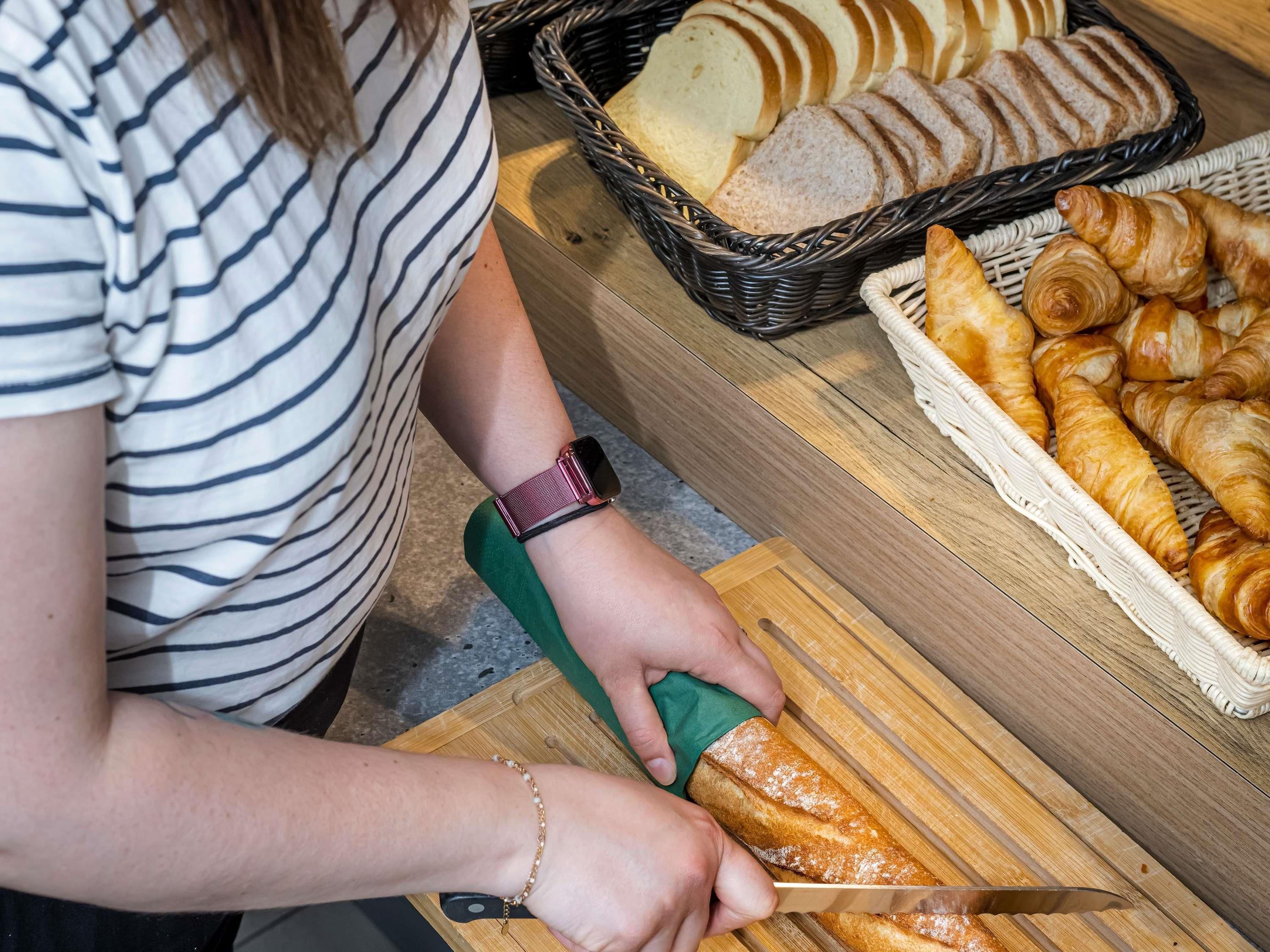 Une personne qui coupe une baguette sur une planche à découper en bois.