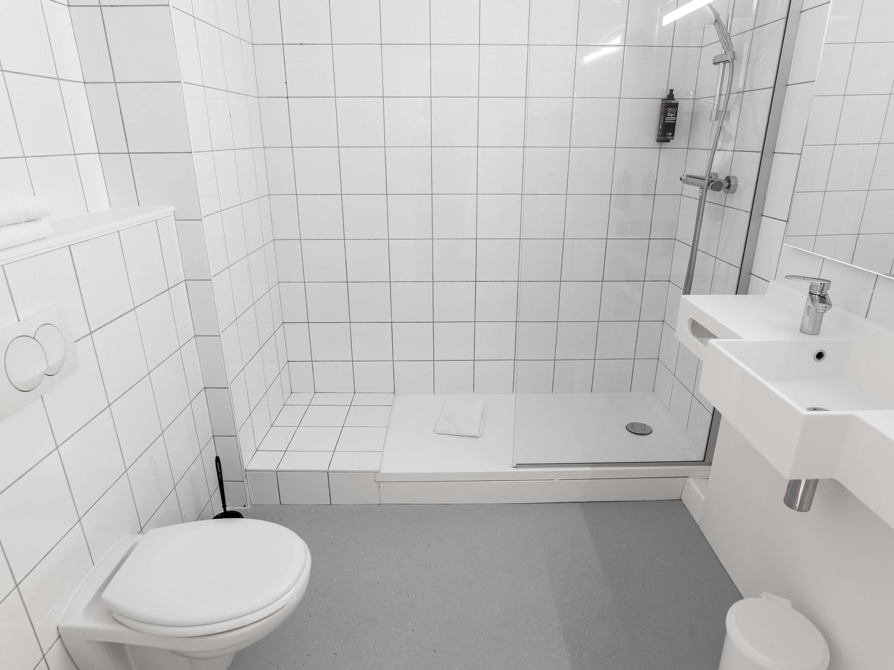 Un bagno moderno rivestito di piastrelle bianche, con water, zona doccia e lavandino.