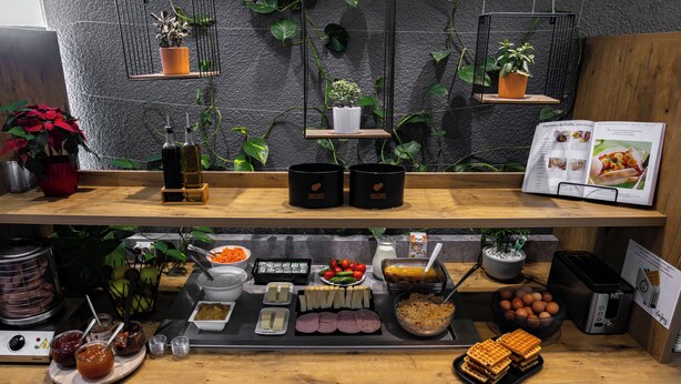 A buffet setup with various food items, a toaster, and potted plants. - ibis budget Strasbourg Sud Illkirch Geispolsheim (Geispolsheim)