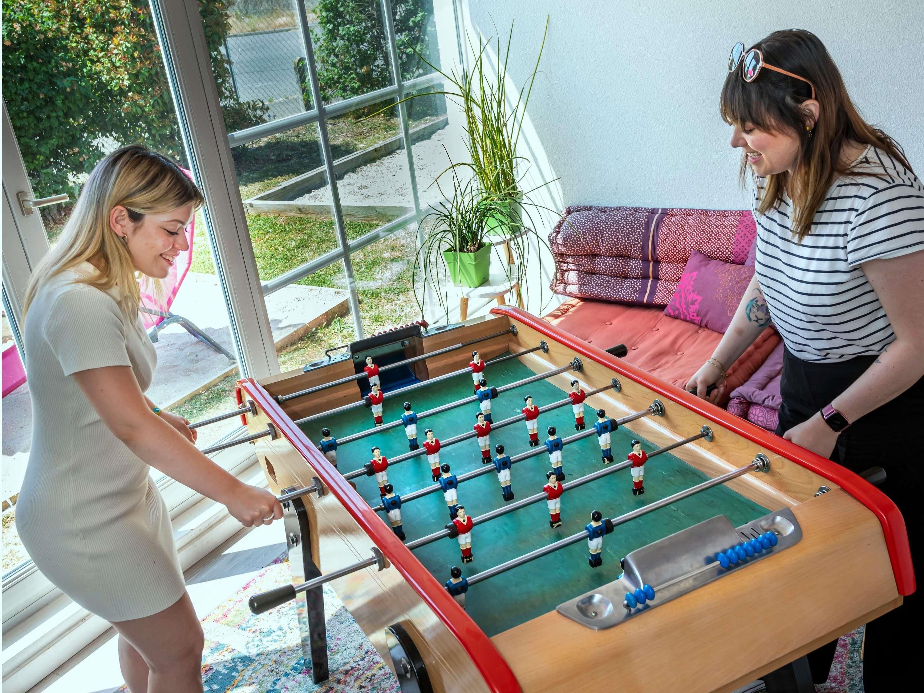 Una mesa de fútbol de mesa en una habitación con un ventanal grande, una planta y un sofá.