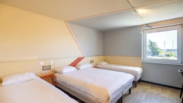 A hotel room with three beds, a window with a view, and a ceiling with exposed ductwork.