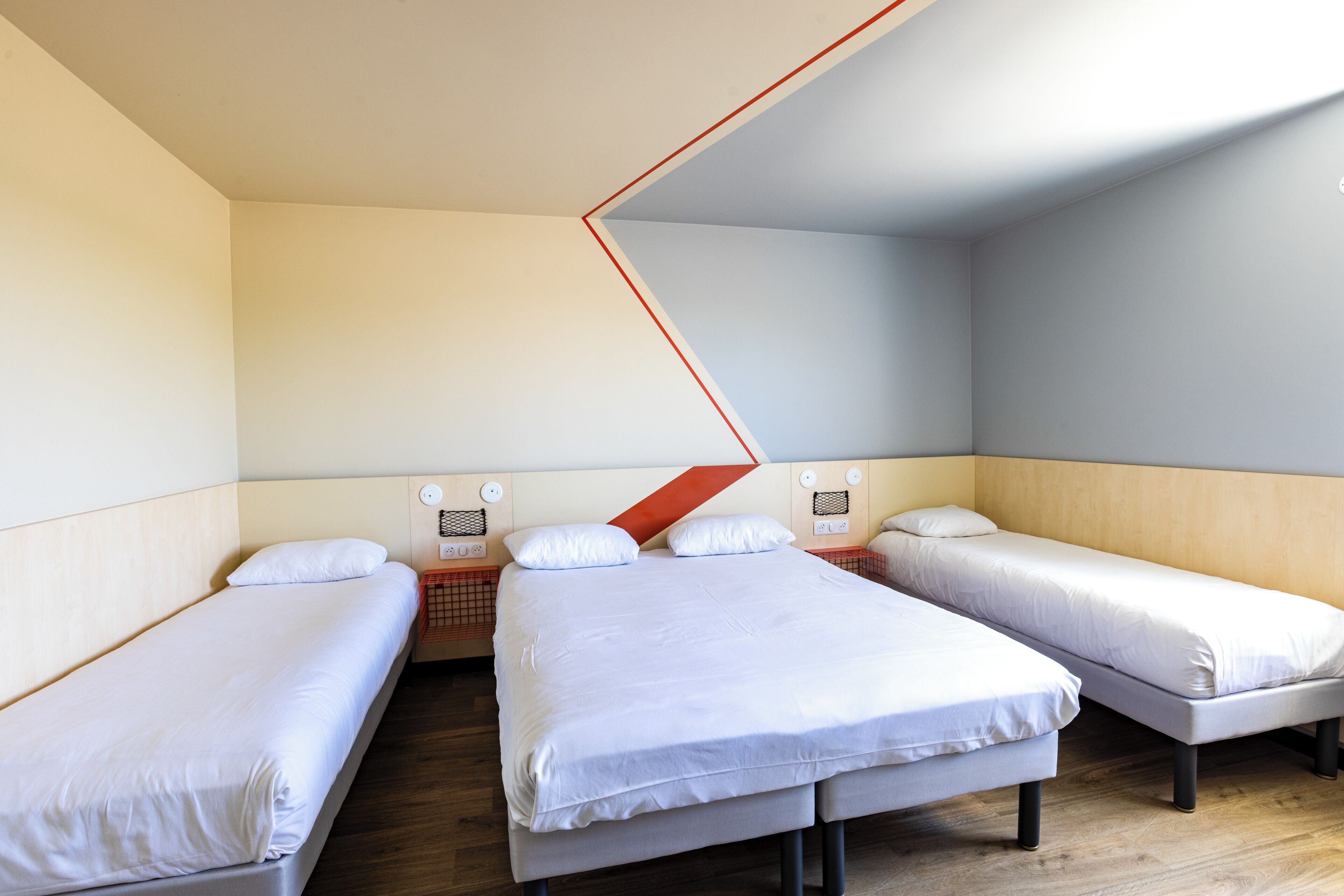 Ein Zimmer mit drei Einzelbetten, Holzboden und schrägverlaufender Decke.