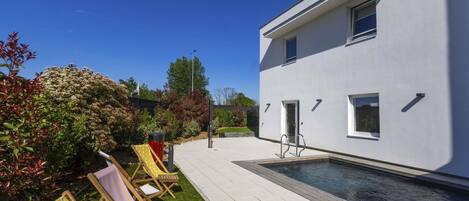Un edificio moderno con piscina, mobiliario exterior y un jardín bien cuidado.