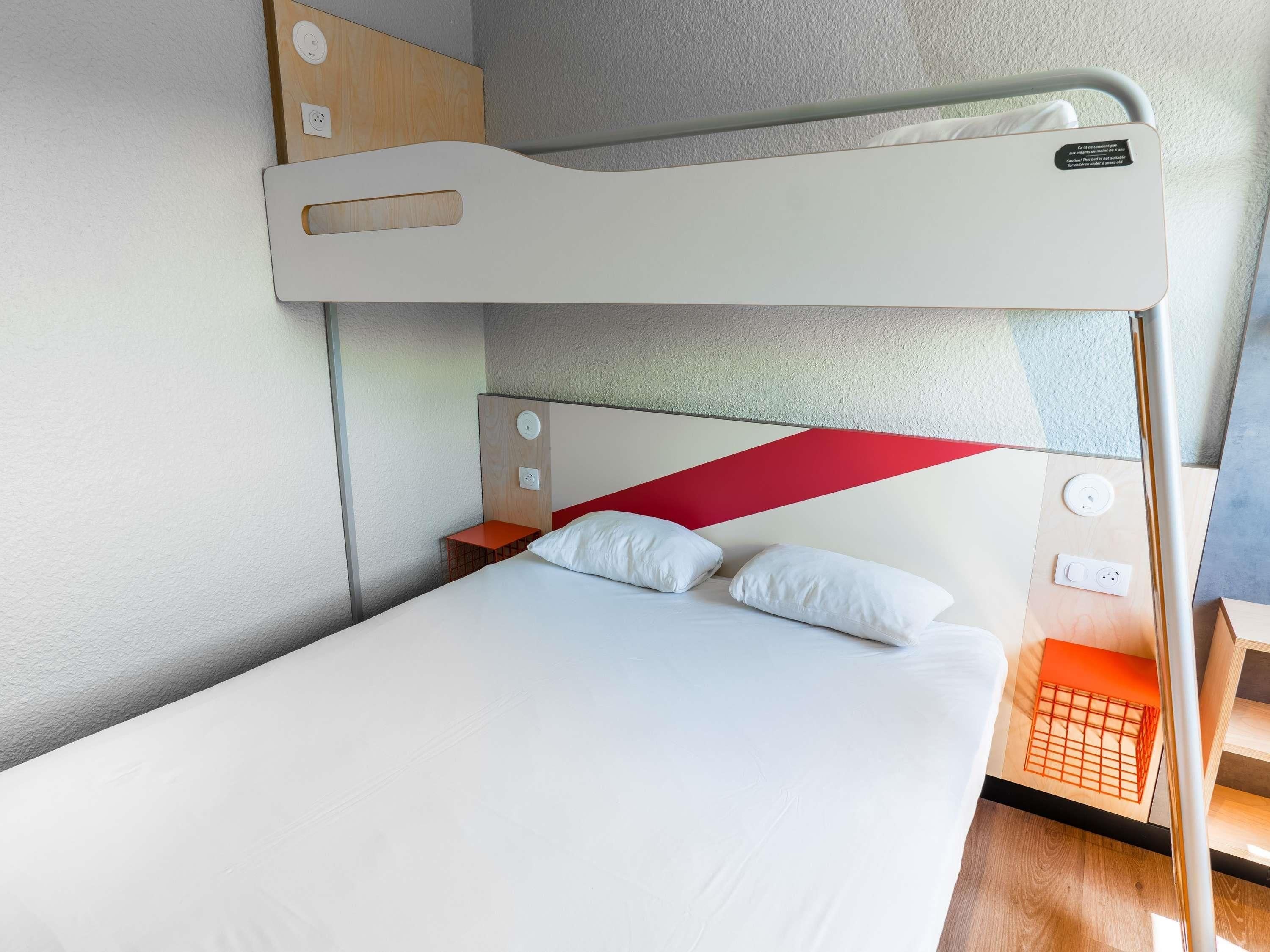 A bunk bed with a red accent, a bedside table, and a power outlet.