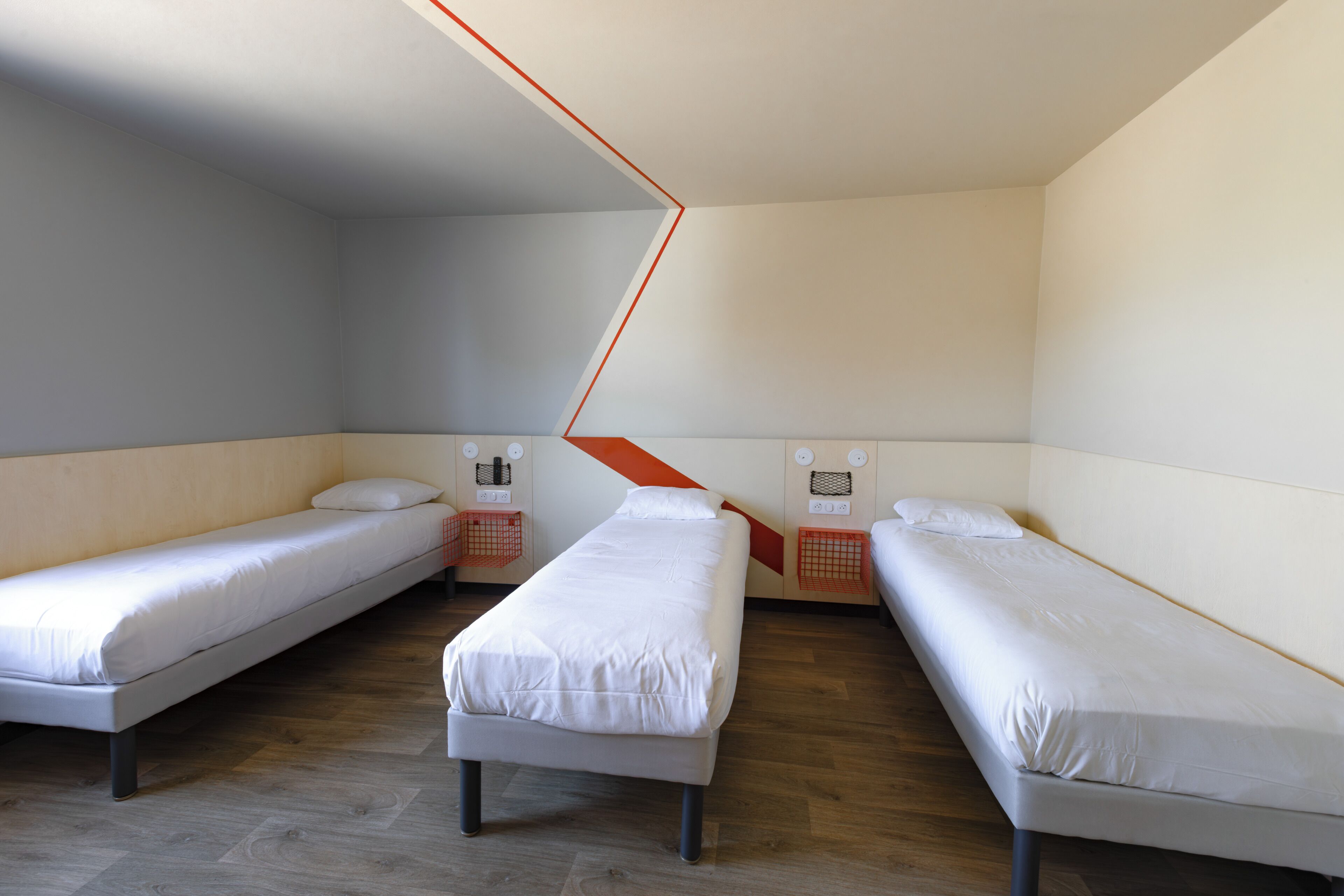 Una habitación con dos camas individuales, piso de madera y techo inclinado.