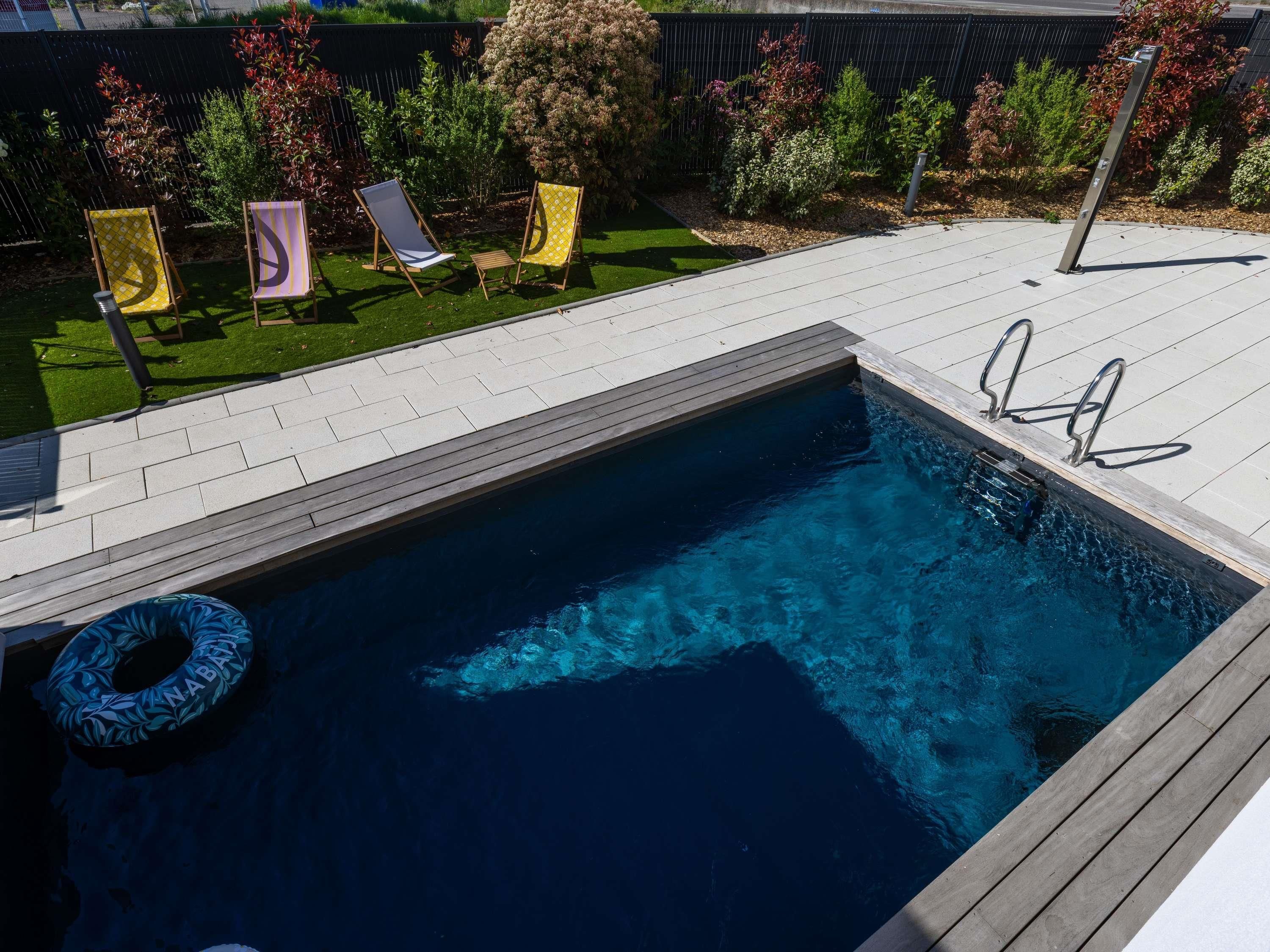 Una piscina con muelle de madera, una silla de descanso y una escalera para la piscina.