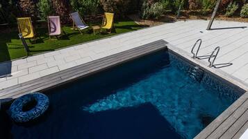 Una piscina con muelle de madera, una silla de descanso y una escalera para la piscina.