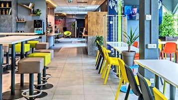 A modern restaurant with high tables and chairs, a bar area, and a seating section with colorful chairs.