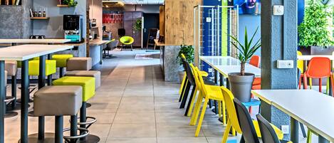 Un restaurante moderno con mesas altas, sillas, una zona de bar y un espacio con sillas coloridas.