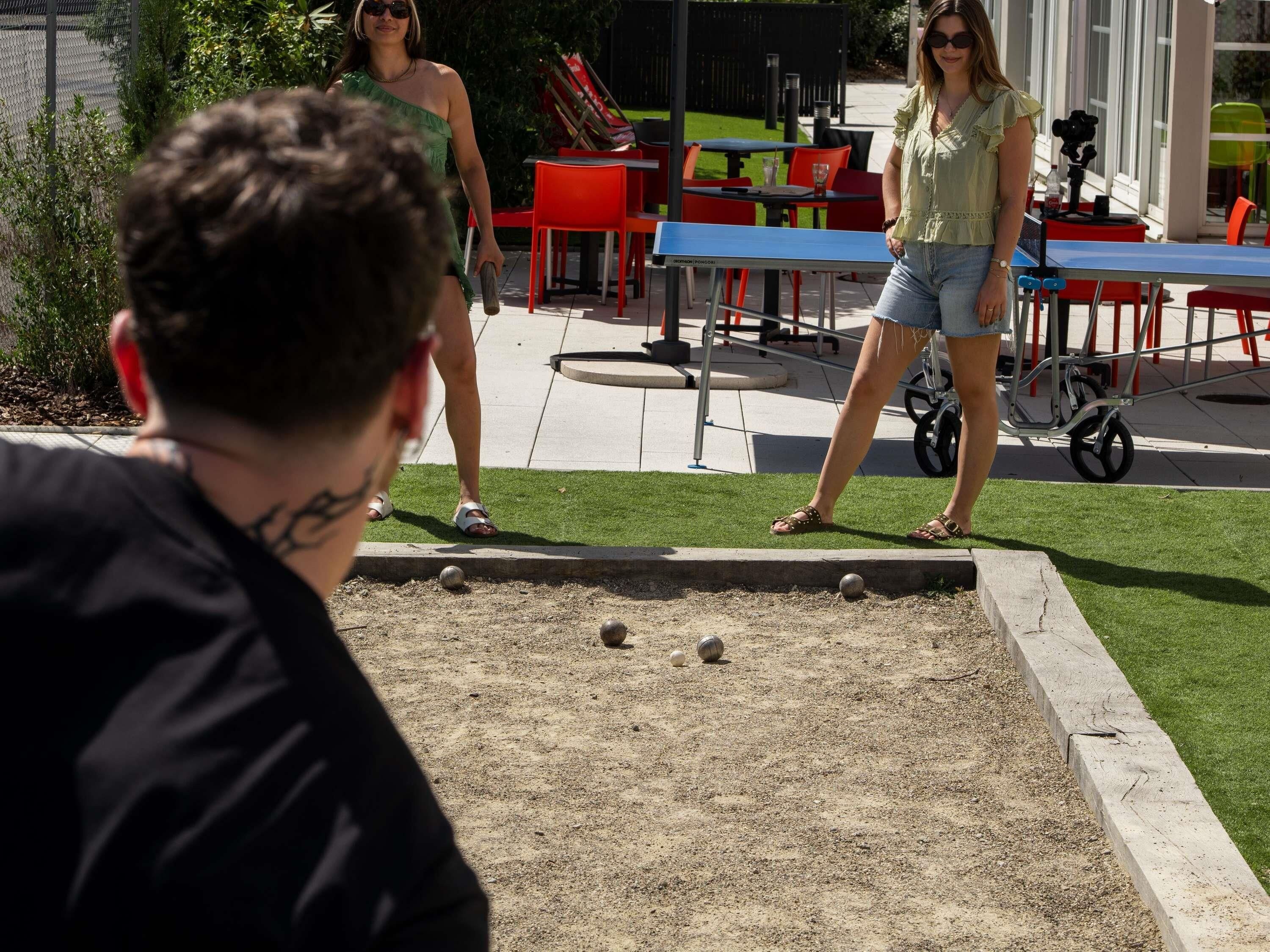 Une table de billard installée à l’extérieur, avec une pelouse verte et des chaises rouges en arrière-plan.