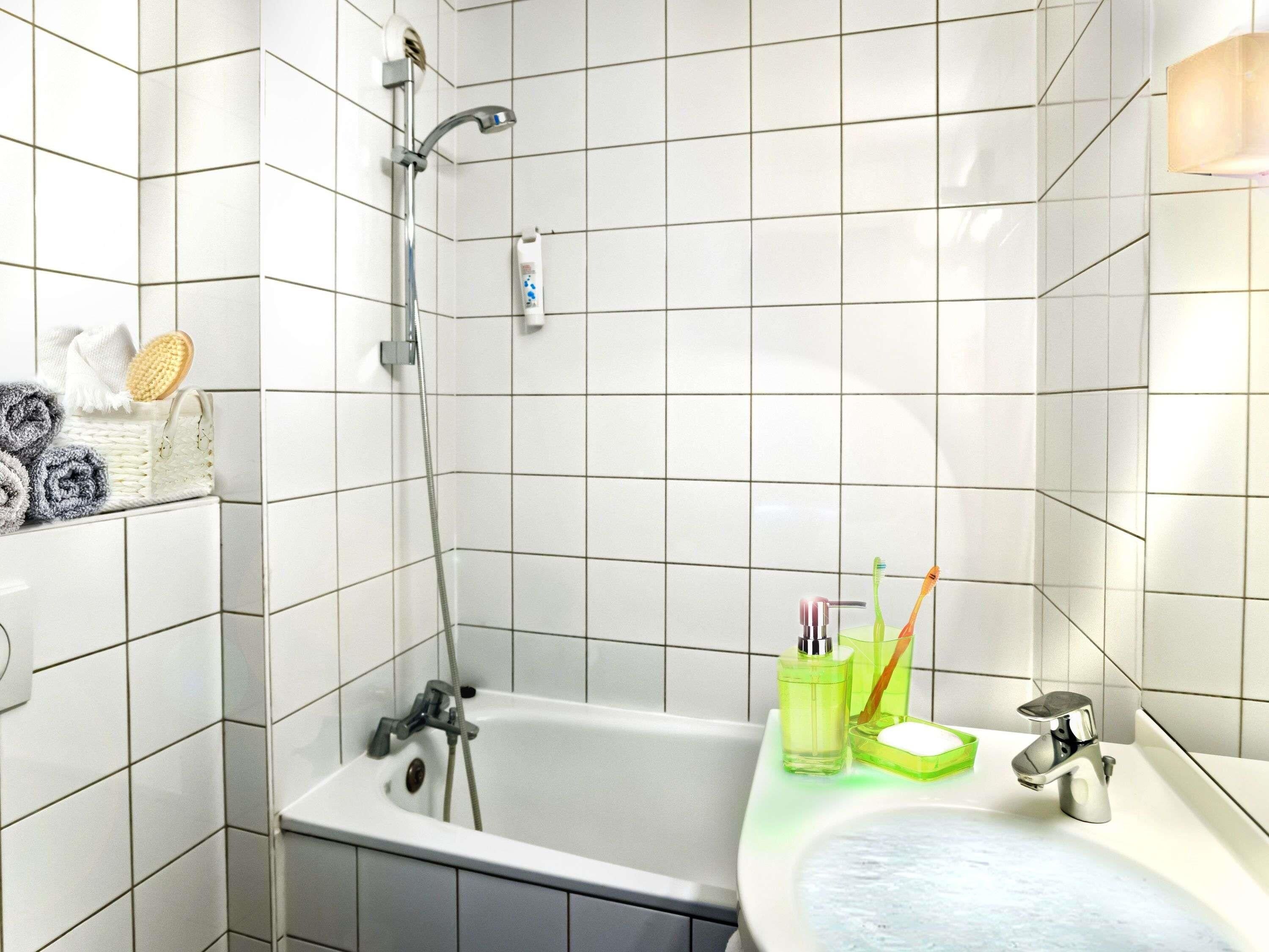Un baño con paredes de azulejos blancos, una bañera, una ducha, un lavabo y artículos de aseo.