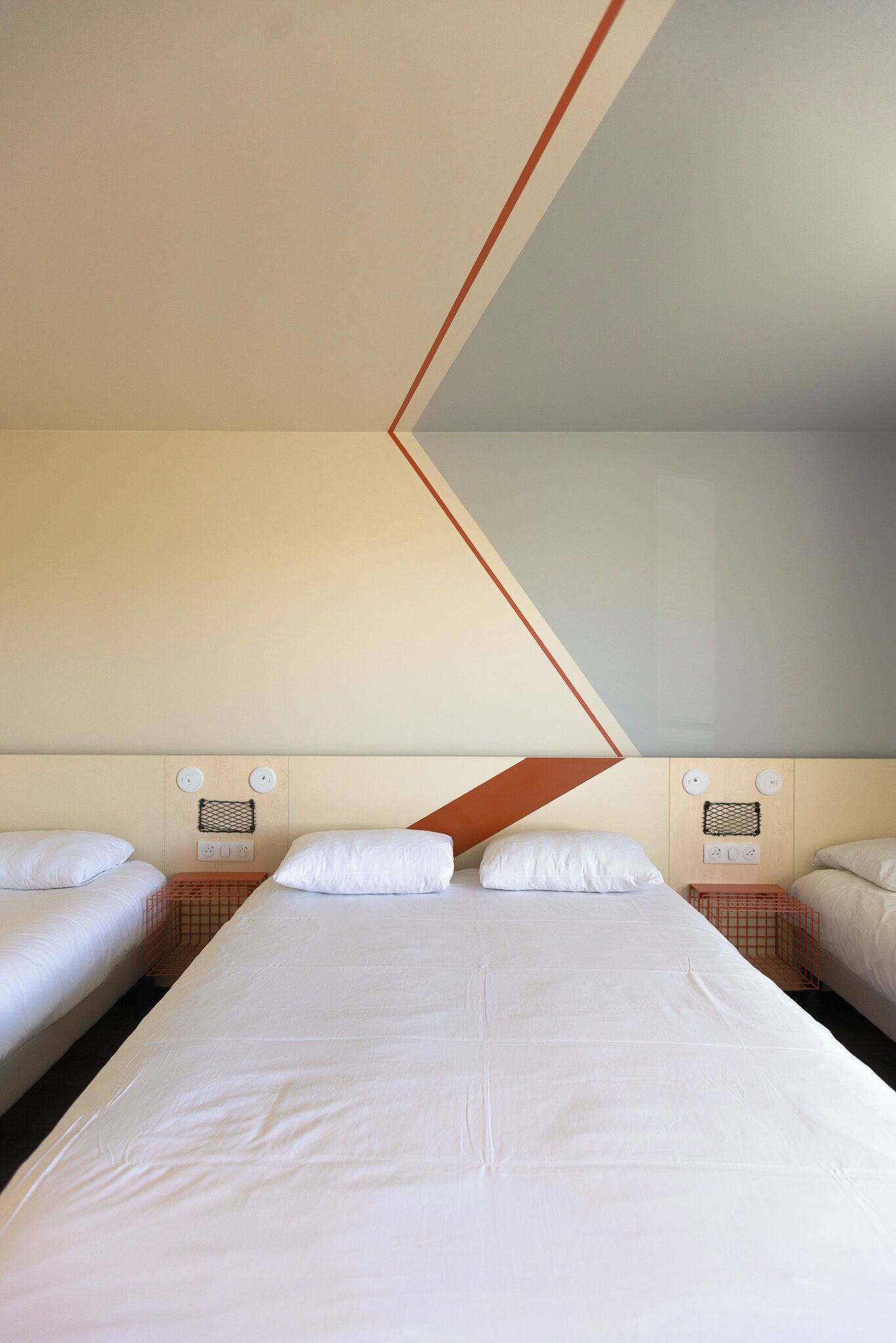 A hotel room with a large bed, two smaller beds, and a geometric wall design.