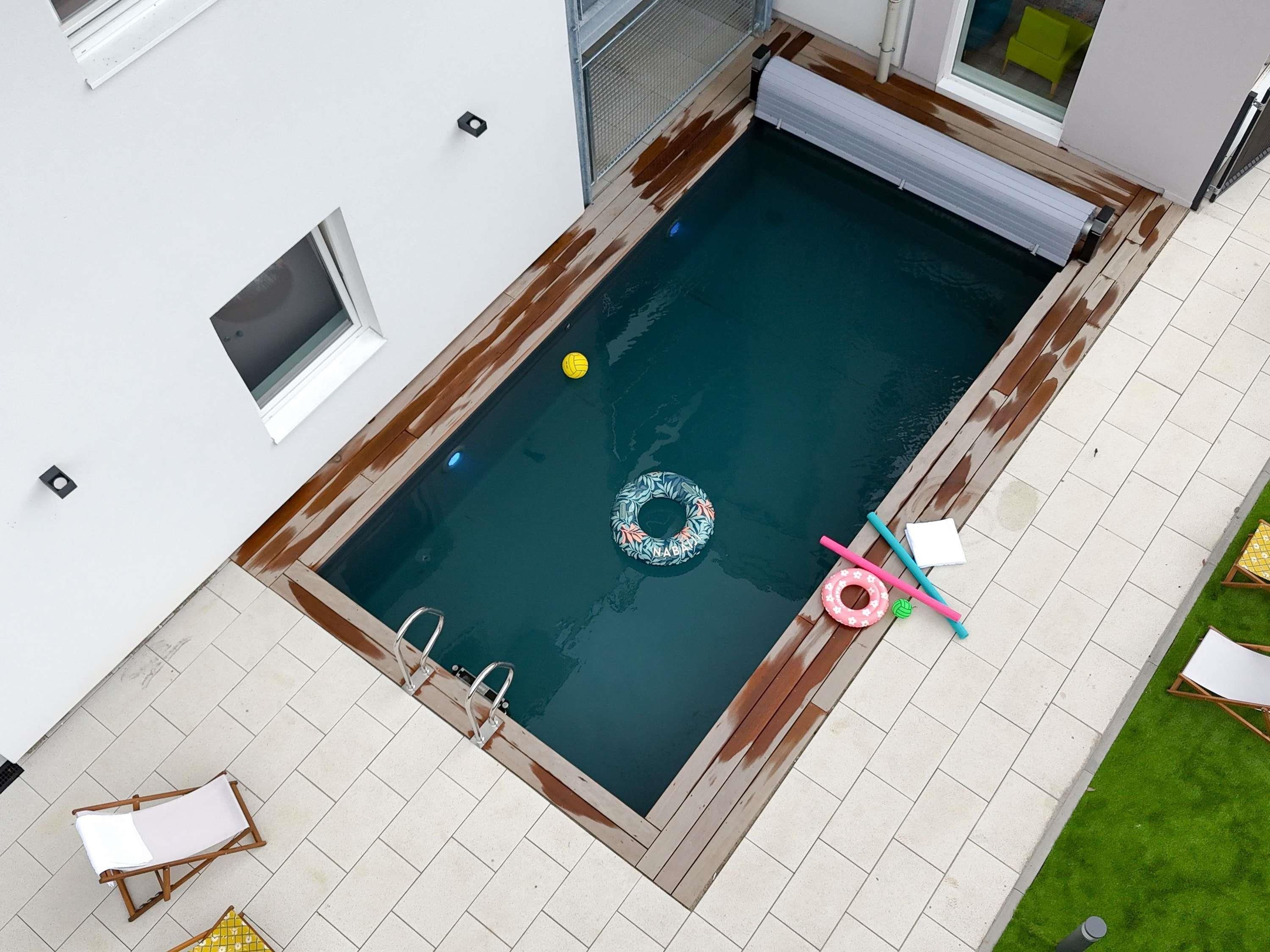A rooftop swimming pool with a wooden deck, a lounge chair, and a small inflatable ring.