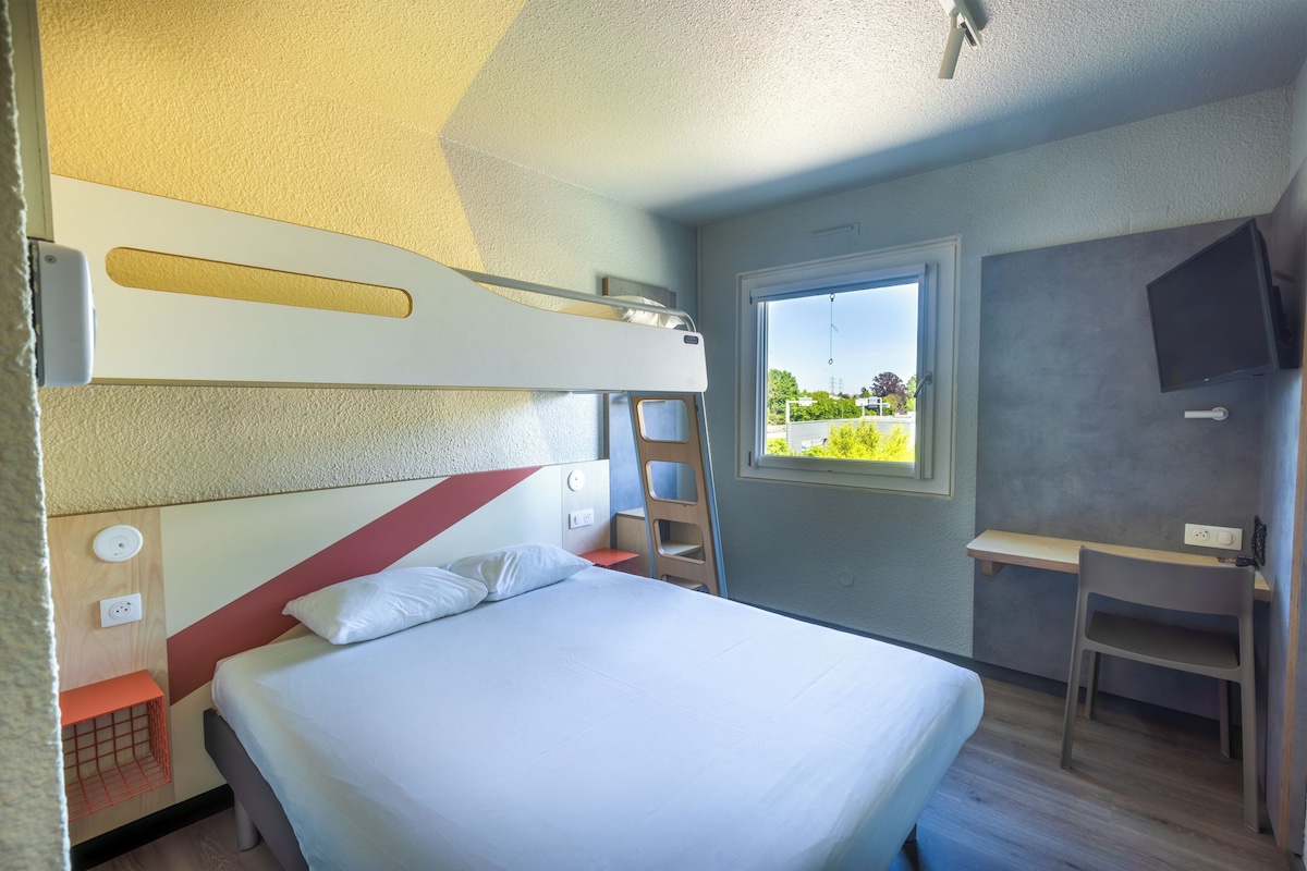Een slaapkamer met een stapelbed, een bureau, een stoel, een televisie en een raam met uitzicht.