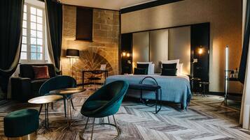 Una habitación de hotel moderna con una cama grande, una zona de estar con una mesa y sillas, una chimenea y un ventanal con cortinas.