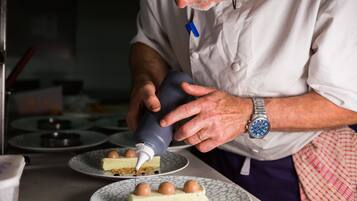 A person in a chef's uniform using a piping bag to decorate a dessert.