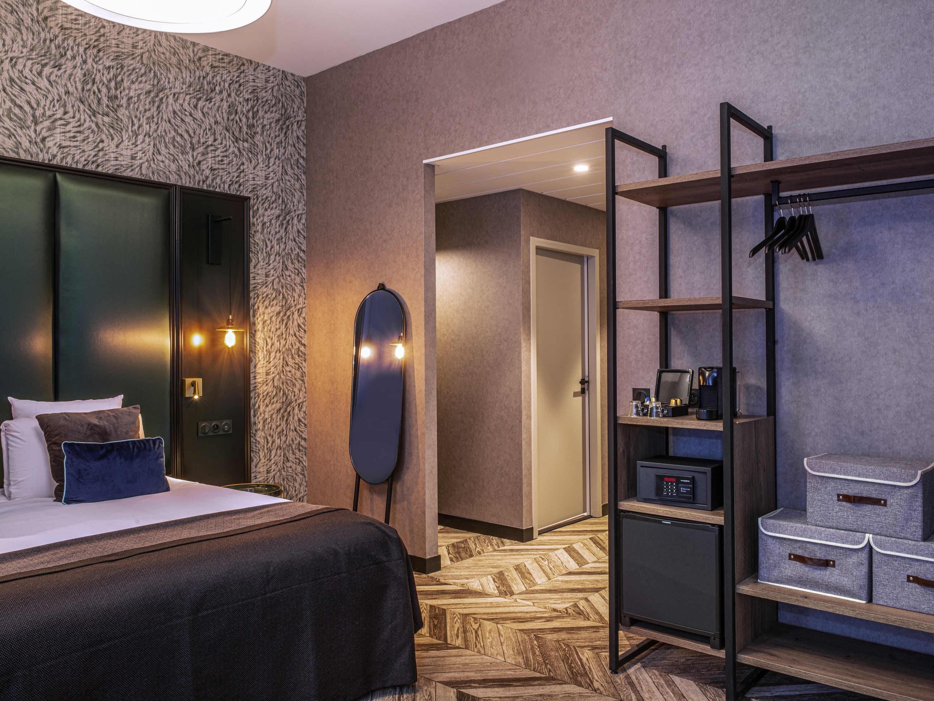 Een hotelkamer met een bed, een kledingkast, een spiegel, een bureau met een computer en een schoenenrek.