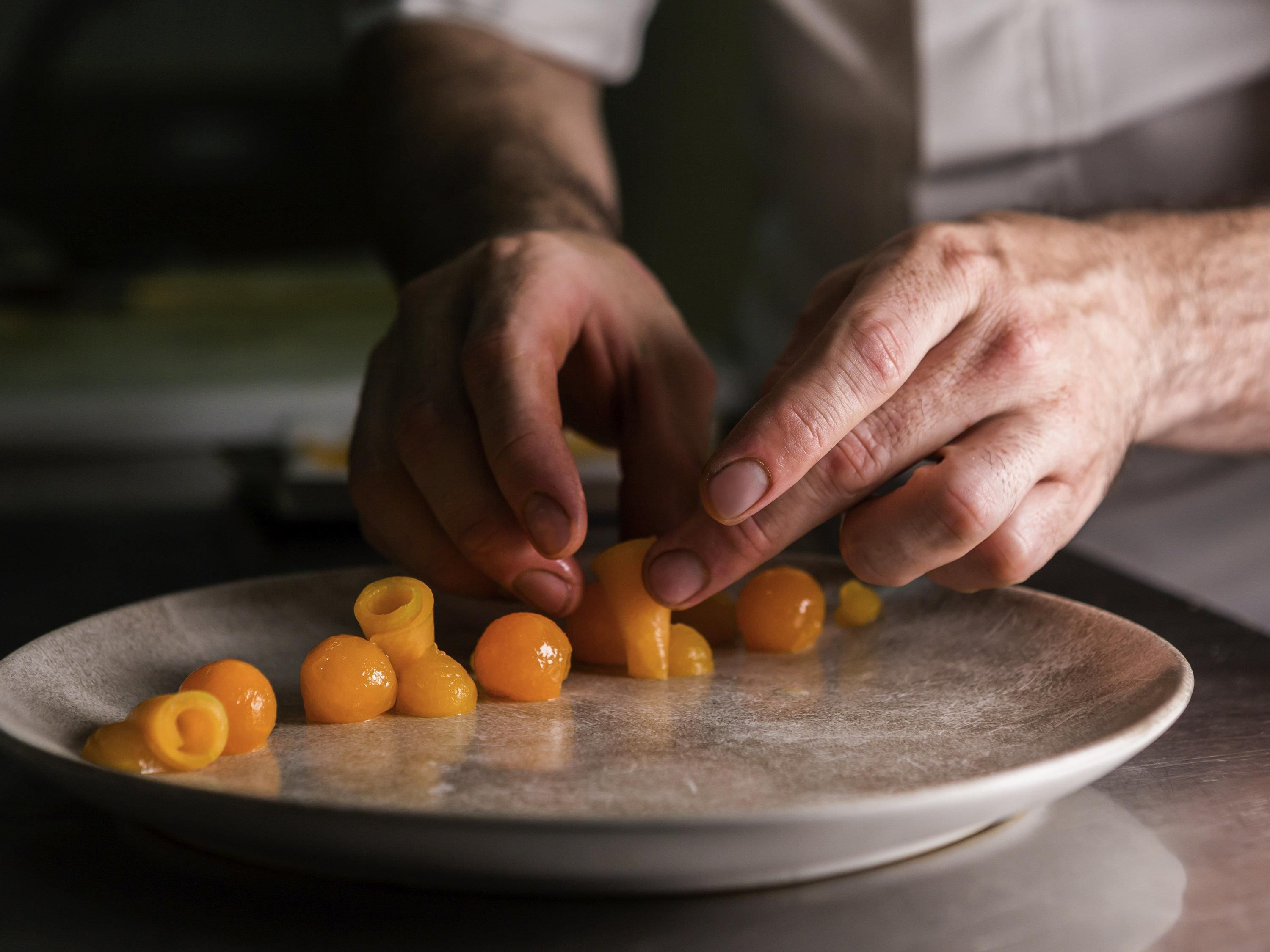 A person handling small, round, orange objects on a plate.