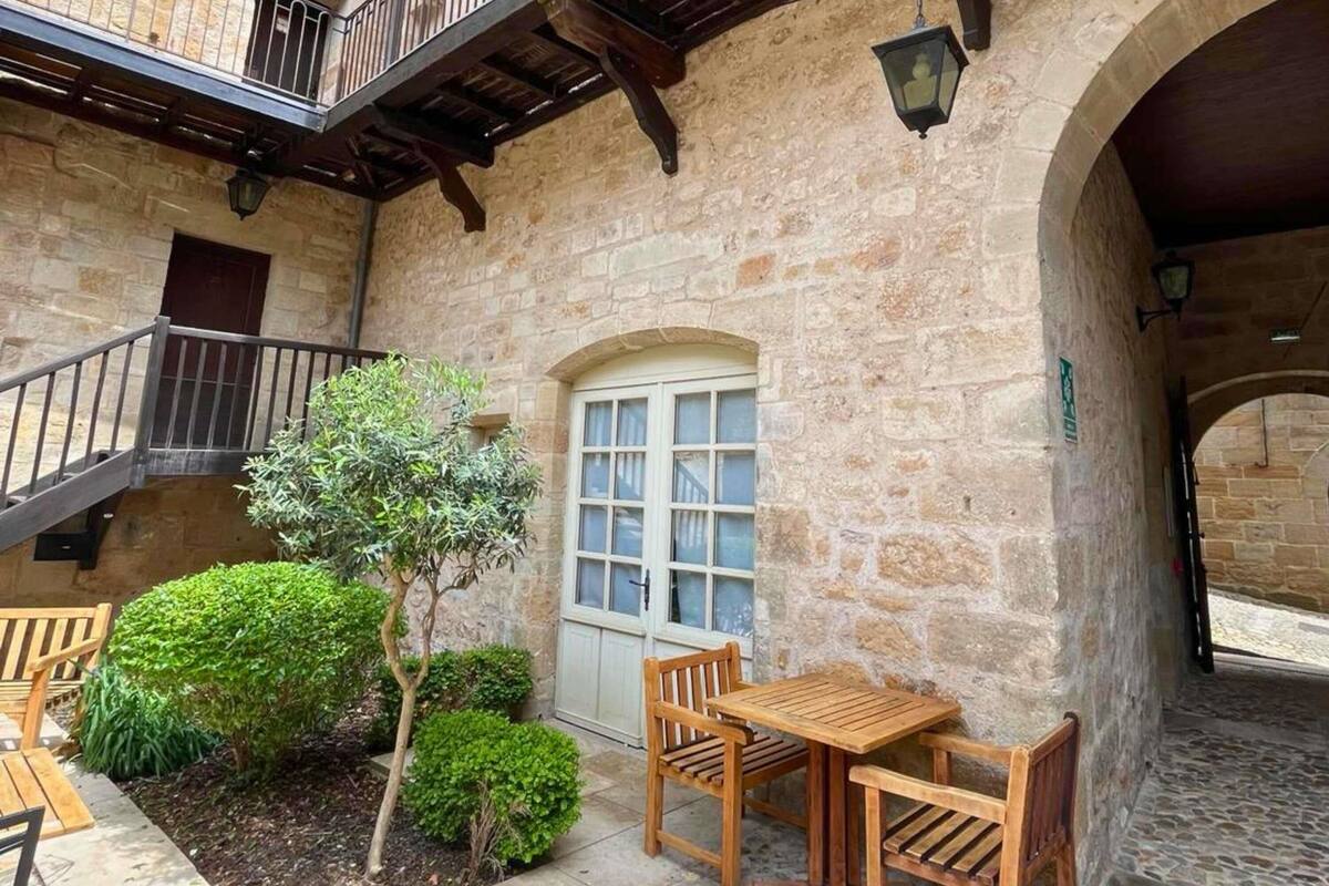 Ein Steinhaus mit einem Holzbalkon, einer Tür und einem kleinen Garten mit Bänken und einem Tisch.