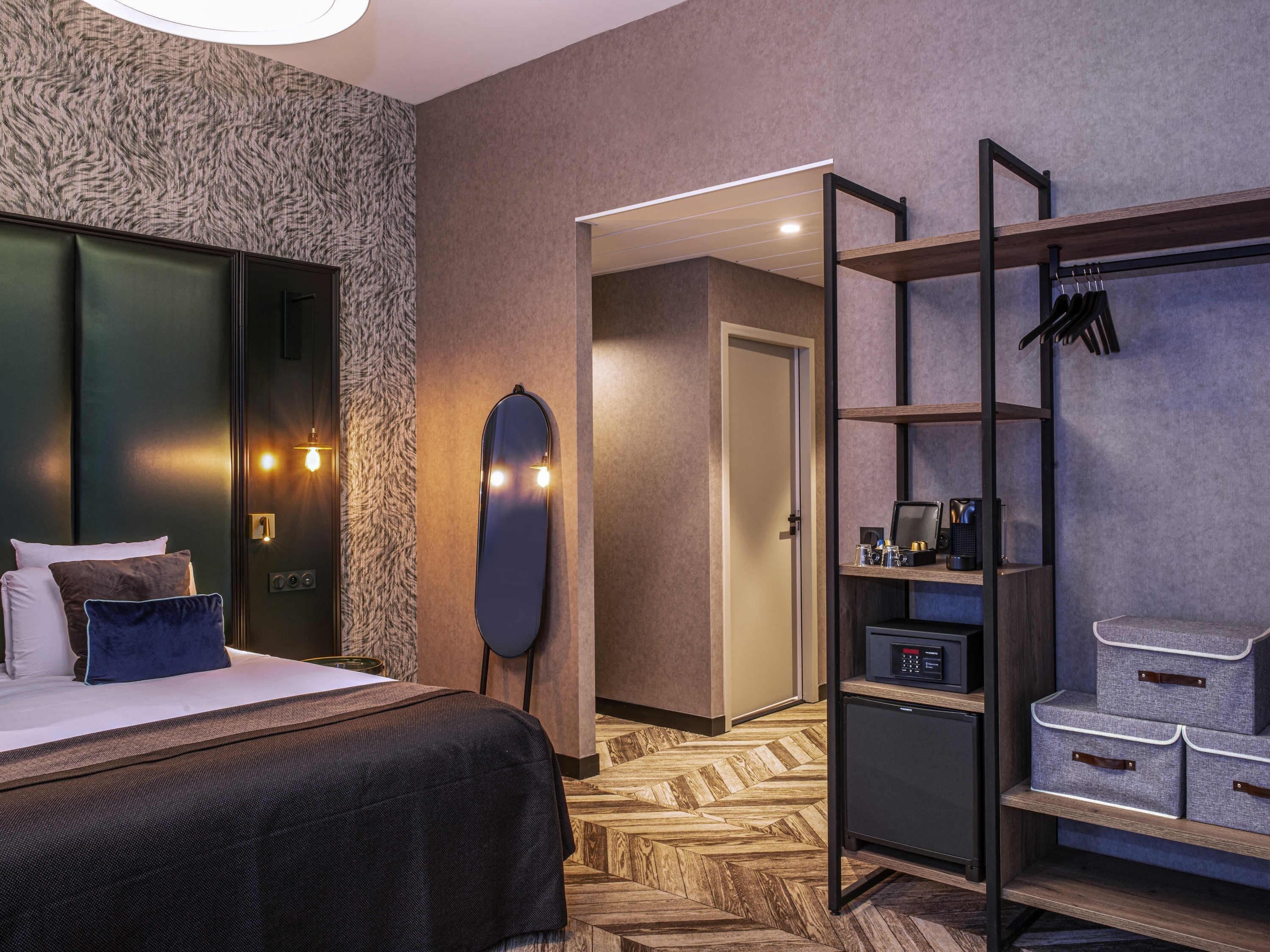 Ein Hotelzimmer mit Bett, Schrank, Spiegel, Schreibtisch mit Computer und Schuhablage.