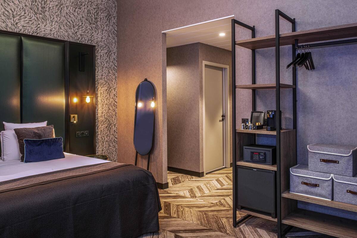 Ein Hotelzimmer mit Bett, Schrank, Spiegel, Schreibtisch mit Computer und Schuhablage.