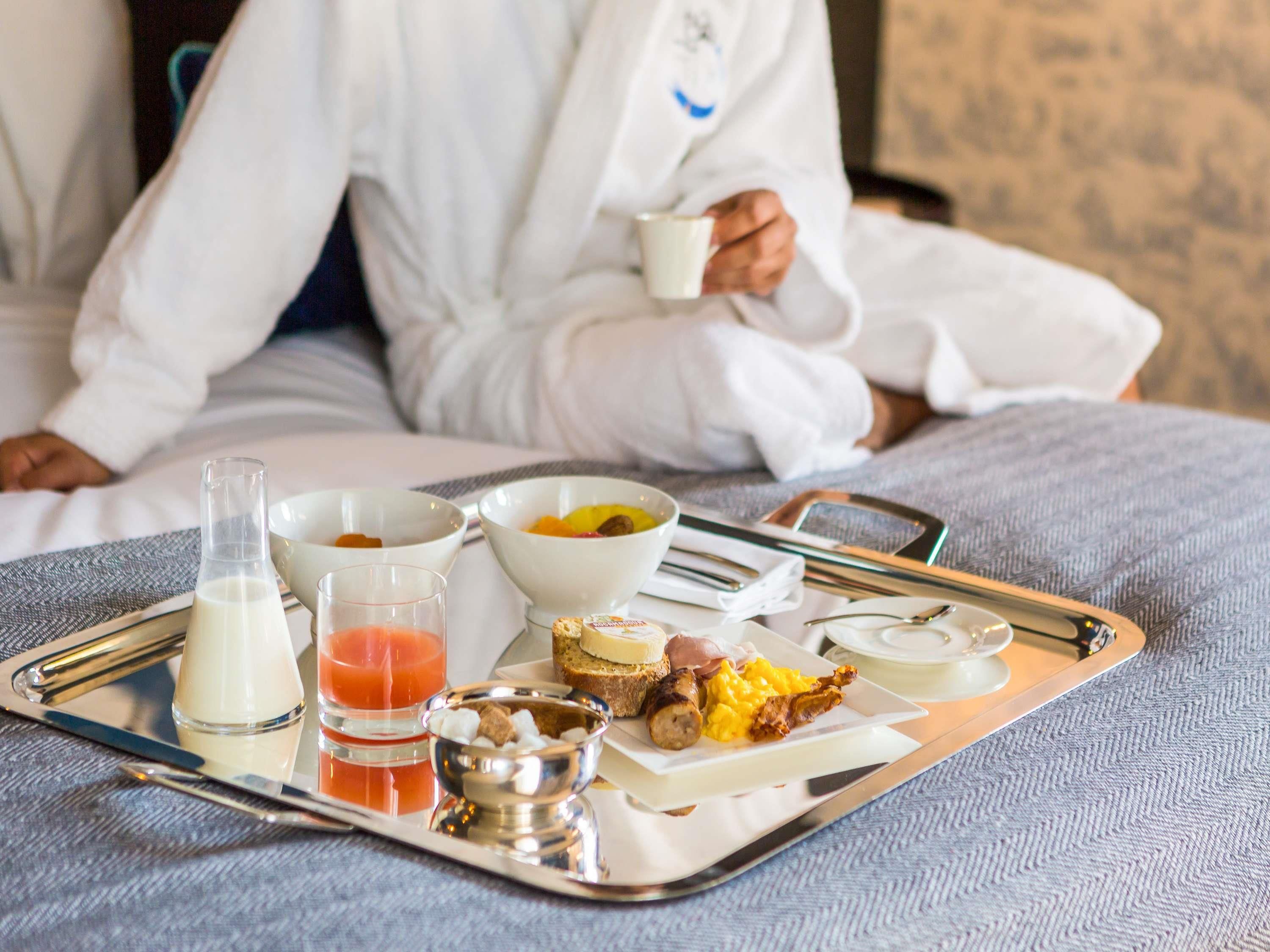 A breakfast tray with milk, juice, eggs, bacon, and toast on a bed.